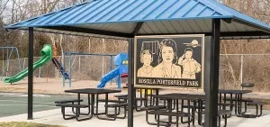 Sign for Rosella Porterfield Park in front of picnic tables under a blue roof