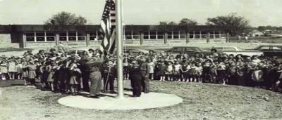 School children and administrators standing around the flag