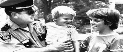 Police officer talking to two children, while holding a baby