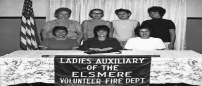 Ladies Auxiliary of the Elsmere Volunteer Fire Dept. standing behind a table and in front of an American flag